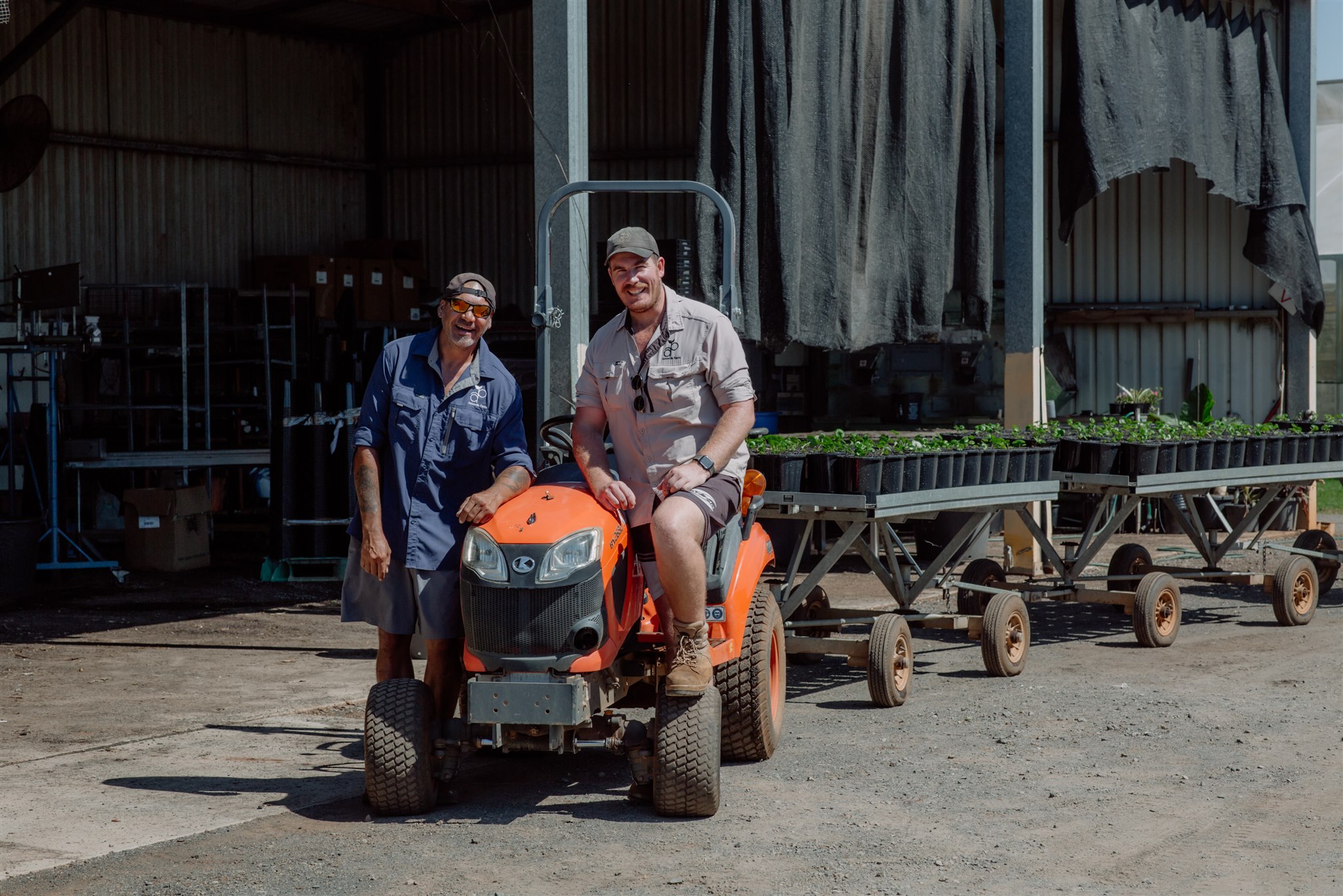 Two smiling Florafolia team members on the nursery tractor with trolleys of young stock